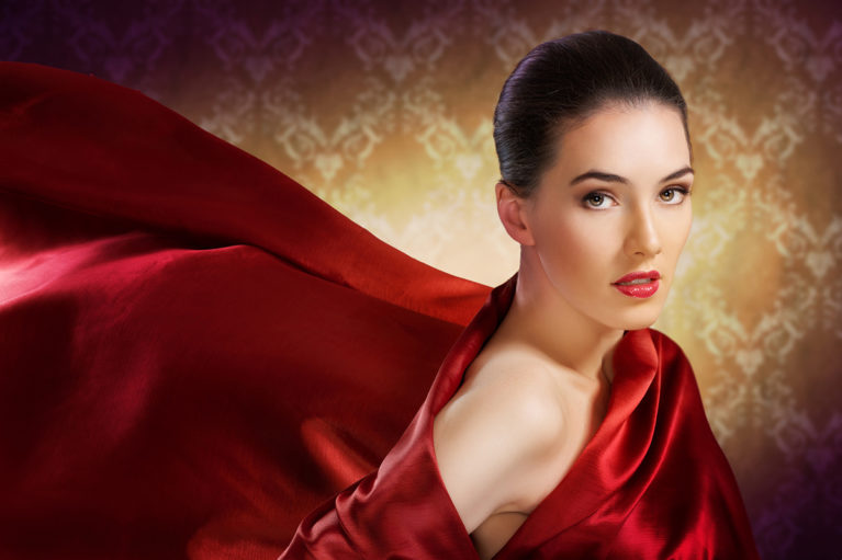 A woman in red silk with a flawless glow and complexion after receiving a vampire facial procedure.