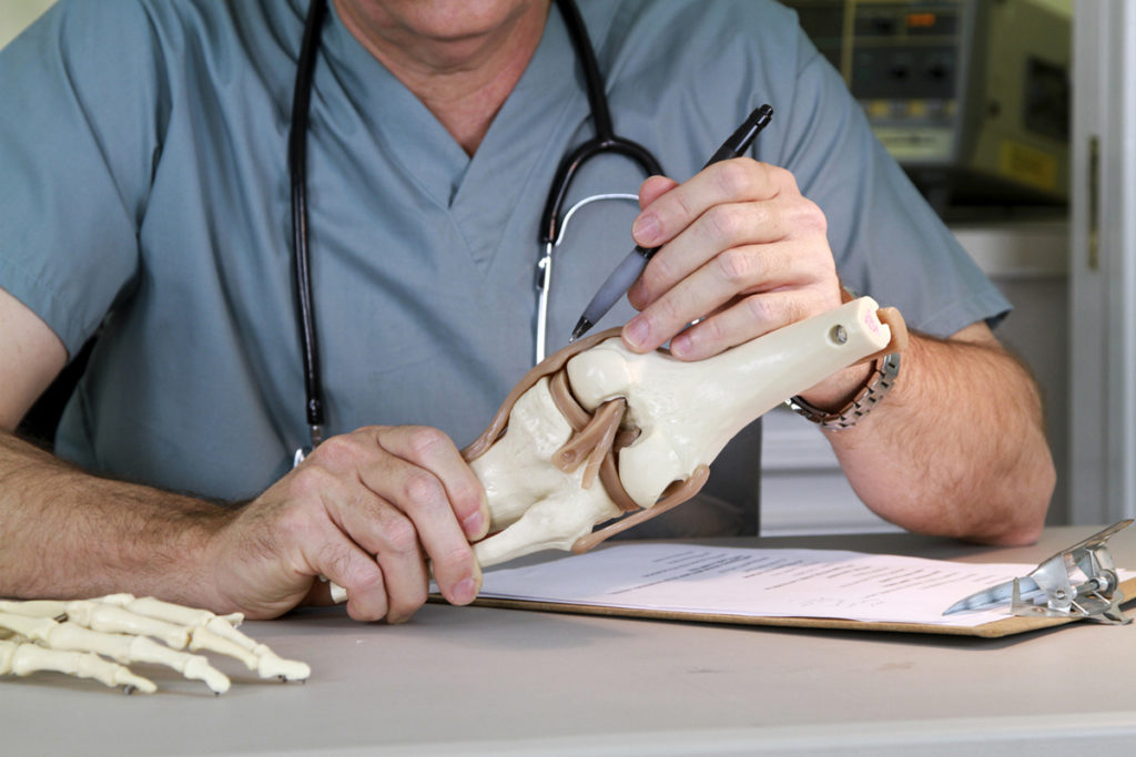 A Naturopathic Doctor marking a model of a human knee joint for a Prolotherapy procedure.