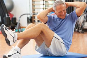 A senior man doing sit ups in a gym, as part of a men's health & wellness plan.